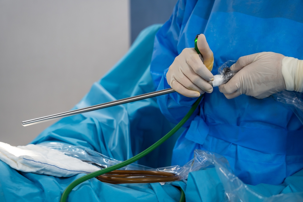 Surgeon in blue scrubs and gloves handling a laparoscopic instrument with a green tubing during surgery.
