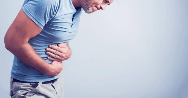 Man in a blue polo shirt hunched over, clutching his midsection in apparent stomach pain.
